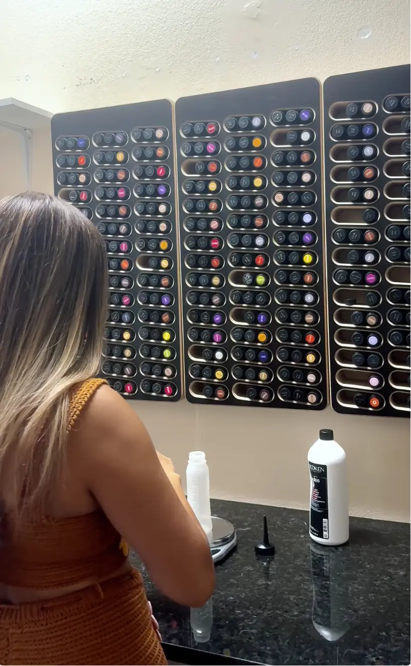 New salon owner mixing hair color I her salon’s back room standing front of her bottles hair color organized by wall mounted Huebar units.