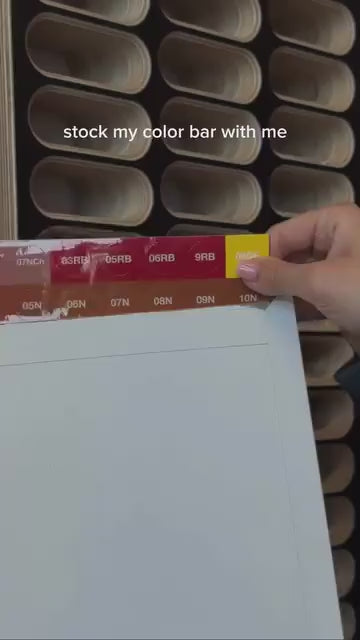 Video of hairstylist labeling her hair color bottles to organize them inside a MCM style wood display organizer with a black laminated front.